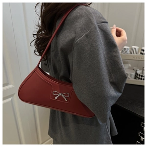 Close-up of red leather underarm bag featuring a metallic silver bow ornament detail