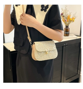 Detailed shot of straw woven crossbody bag featuring white floral lace embroidery and gold lock
