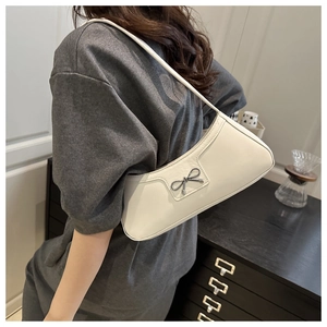 Detail of white half-moon underarm bag with silver metal bow charm on leather strap