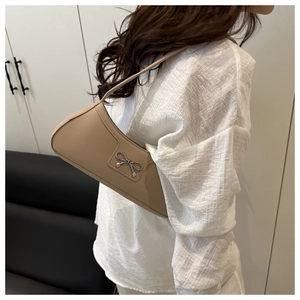 Close-up of khaki crescent bag with silver metal bow worn as an underarm shoulder bag
