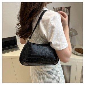 Detail of black faux crocodile leather baguette bag worn as an underarm shoulder bag