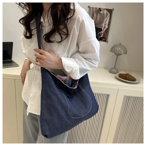 Detail view of a large navy denim crossbody bag with a curved front pocket and patterned lining