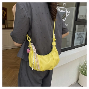 Street style view of yellow crescent bag with heart charm and woven rope decoration