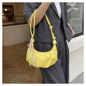 Detail of a bright yellow pleated hobo bag with a woven charm and heart pendant