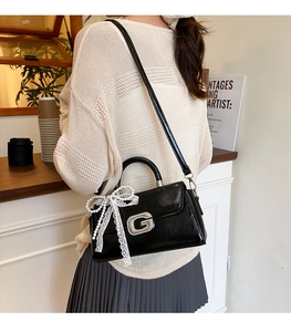 Detail of glossy black leather handbag featuring a diamond G buckle and pearl lace bow