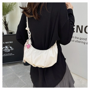 Detail of creamy white crescent shoulder bag with pleated leather and pink heart charm