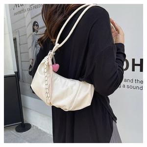 Close-up of cream crescent shoulder bag with pleated details and heart pendant charm
