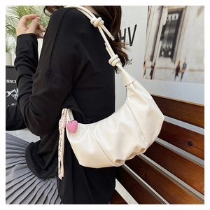 Detail of off-white pleated dumpling bag with knotted strap and pink heart charm