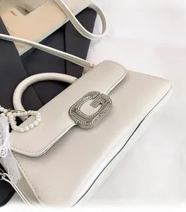 Detail of off-white crossbody bag with G-shaped rhinestone buckle and pearl lace chain