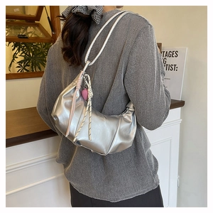 Detail of silver metallic crescent underarm bag with pleated texture and heart charm