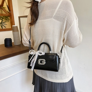 Detail of black patent leather handbag with silver G buckle and pearl lace bow accessory