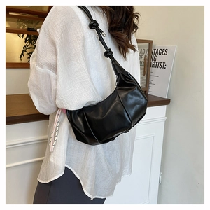 Close-up of black ruched cloud bag with decorative knot strap detail in a minimalist setting