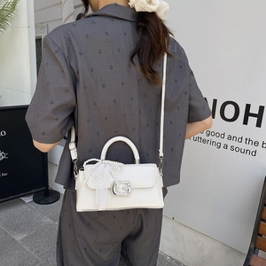 Detail of white glossy leather handbag featuring pearl chain and lace bow with metal G buckle
