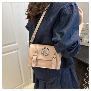 Detail showing beige mini crossbody bag with metal M logo and stylish buckle straps