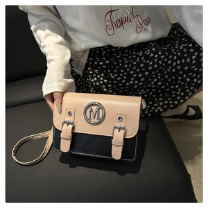 Détail du sac bandoulière bicolore avec un logo M argenté et des boucles décoratives