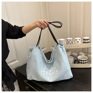 Détail du sac cabas en denim bleu clair avec broderie Hello et cordon de serrage