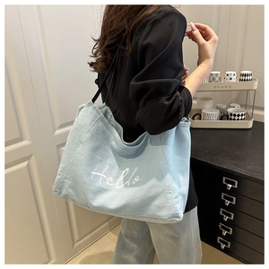 Detail of light blue denim tote bag with white Hello embroidery worn on shoulder