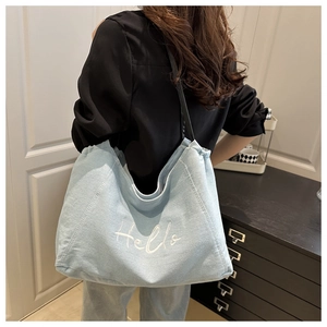 Detail view of light blue denim tote bag with white Hello embroidery and black shoulder straps