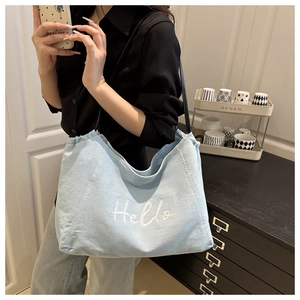 Detail of light blue denim tote bag with white Hello embroidery and ruffled edge design