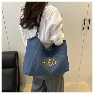 Gros plan sur la broderie jaune Hello du grand sac cabas en denim bleu foncé