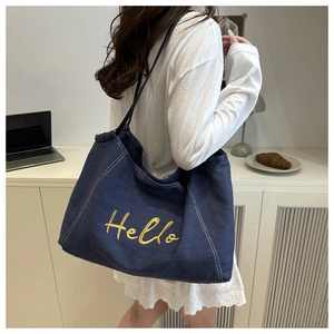 Close-up of dark blue denim tote bag with yellow Hello embroidery worn by model