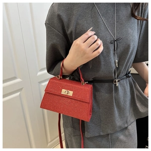 Detail of red textured leather handbag with metal turn-lock and top handle strap