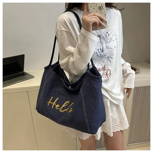 Detail of dark blue denim tote with yellow Hello embroidery and black strap worn by model