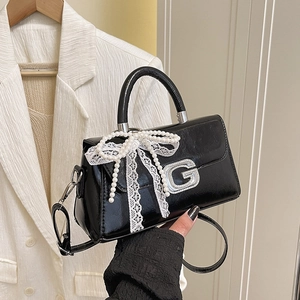 Close-up of black patent leather bag featuring lace bow, pearls, and silver G-buckle detail