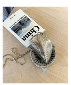 Close-up of silver shell-shaped evening bag with snake chain on a wooden desk