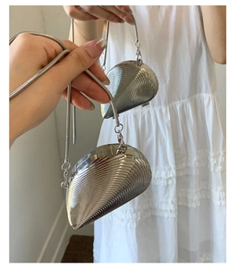 Detailed view of a silver shell-shaped evening bag with wavy metal texture and chain strap