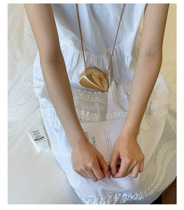 Close-up of a mini gold shell-shaped crossbody bag with a delicate metal chain strap