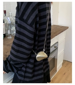 Golden shell-shaped clutch bag with spiral texture and chain strap worn by a model