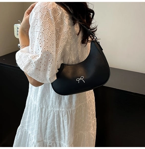Detail of black hobo shoulder bag with a silver metal bow accent on white lace dress