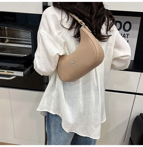 Close-up of a beige faux leather hobo bag featuring a silver metal bow detail and slim strap