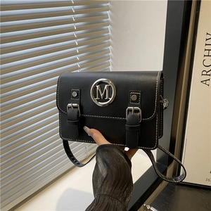 Sac sous le bras noir chic avec logo M argenté et surpiqûres sur un bureau blanc moderne