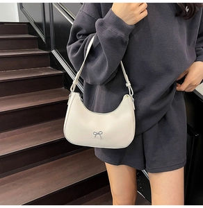 Detail of cream crescent shoulder bag with silver bow accent and adjustable strap