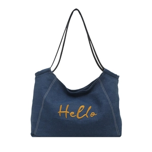 Deep blue denim tote bag with yellow Hello embroidery and slim black straps on white background