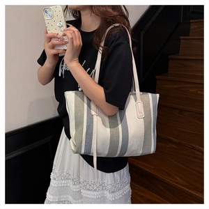 Vertical striped canvas tote bag in beige and blue shown being carried on shoulder