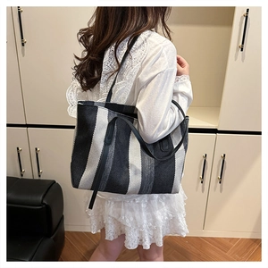 Detailed view of large striped woven tote bag featuring black leather shoulder straps