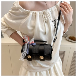 Detail of black woven cylinder bag with gold clasps and decorative lace bow charm