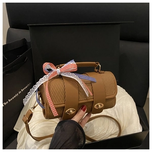 Close-up of brown woven cylinder bag with gold lock and decorative lace bow ribbon