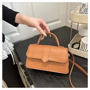 Detail of tan brown textured flap handbag with semi-circular handle and gold hardware