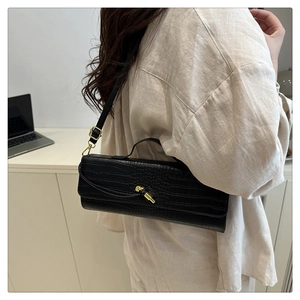 Detail of black crocodile texture baguette bag with golden buckle and sleek leather strap