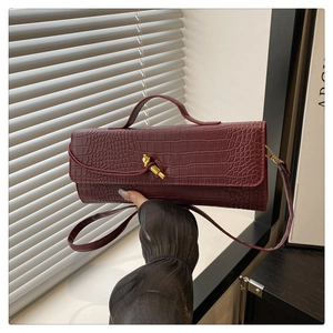 Detailed view of crocodile pattern burgundy baguette bag with a golden metal twist lock