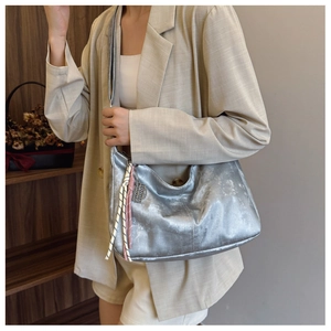 Close-up of silver metallic hobo bag with colorful woven tassels and zip detail