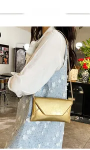 Close-up of golden envelope-style chain bag worn cross-body with metallic stripe texture