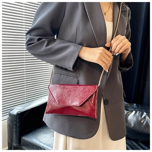 Detail of wine red oil wax leather crossbody envelope bag with gold chain strap on model