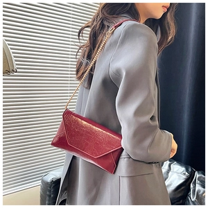 Detail der roten glänzenden Lackleder-Umschlagtasche mit goldener Kette am Model