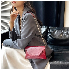 Detail of dark red envelope bag with glossy wrinkled leather and fine gold chain strap