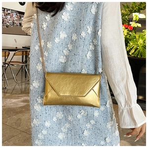 Detail of a gold envelope crossbody bag with metallic finish and thin gold chain strap